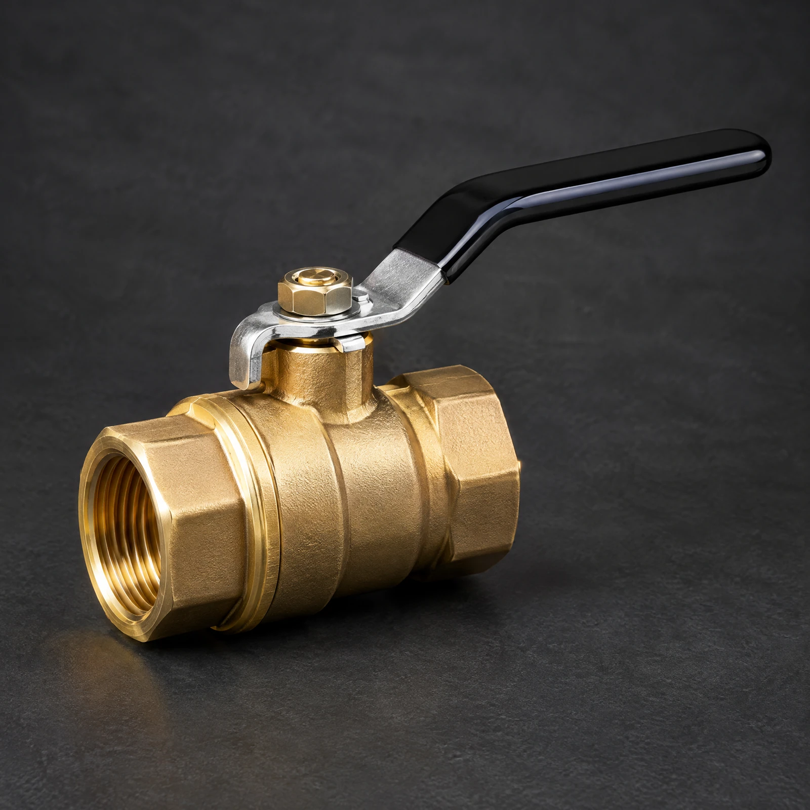Gold-tone ball valve with a black lever handle and female threaded ends on a dark slate surface