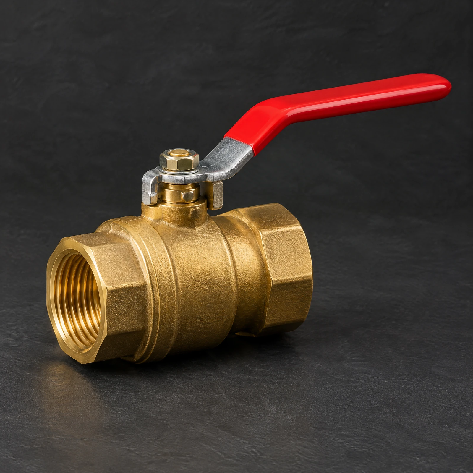 Gold-tone ball valve with a long red lever handle and female threaded ends on a dark slate surface