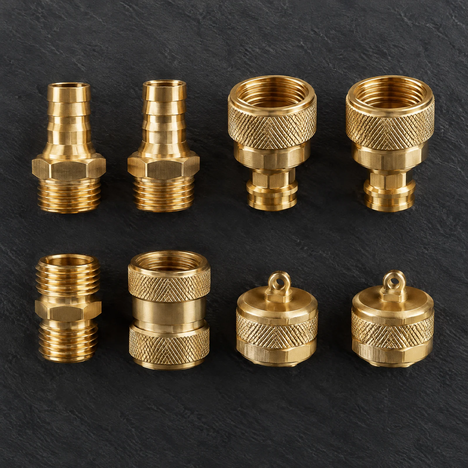 Eight brass-colored garden hose fittings including barbed ends, knurled connectors, couplers and caps on a dark slate surface